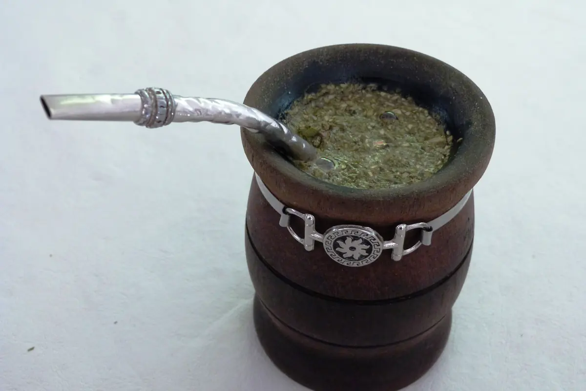 A wooden mate gourd with a silver-banded rim, filled with yerba mate and a silver bombilla straw
